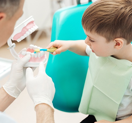 Dentist showing child how to brush teeth at children's dentistry visit