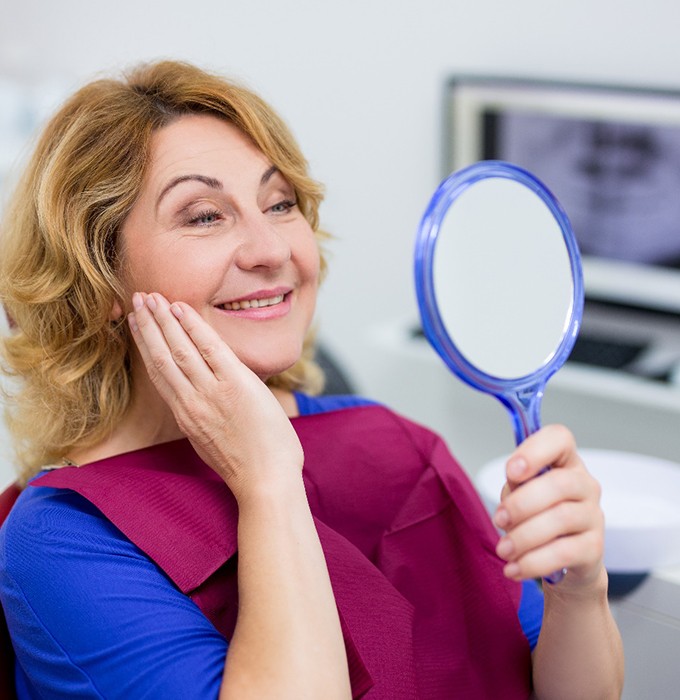 woman admiring her smile in a hand mirror in dental chair 