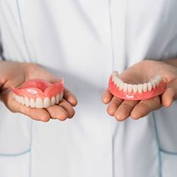 Person in white coat holding full set of dentures