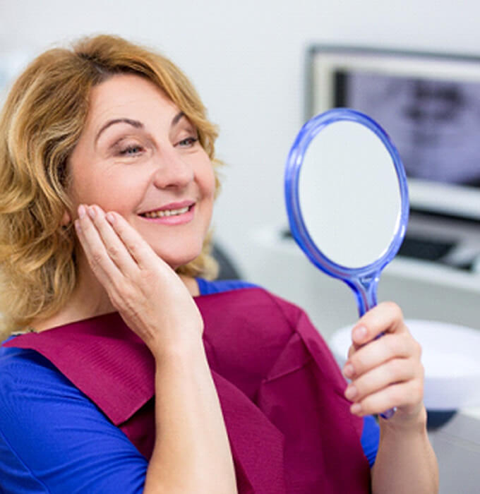 An older woman admiring her smile in a hand mirror