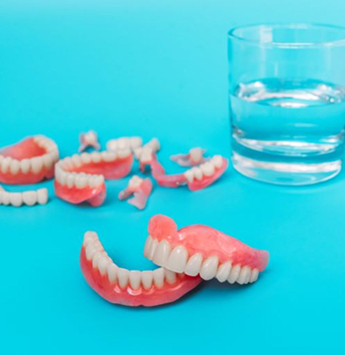 Multiple dentures arranged next to a glass of water