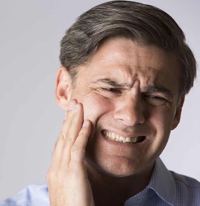 Man in need of emergency dentistry holding cheek in pain