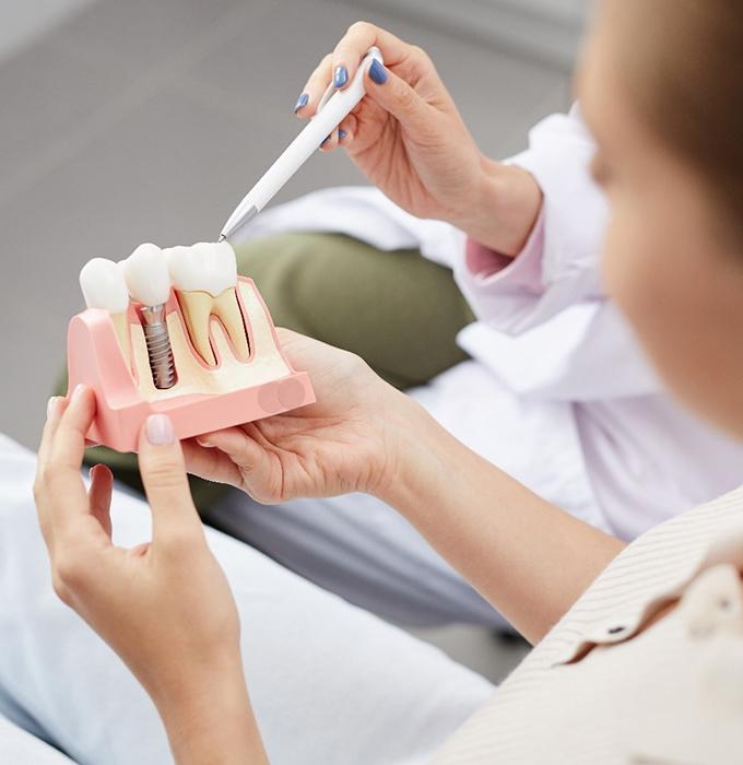 a dentist showing a patient a model of a dental implant