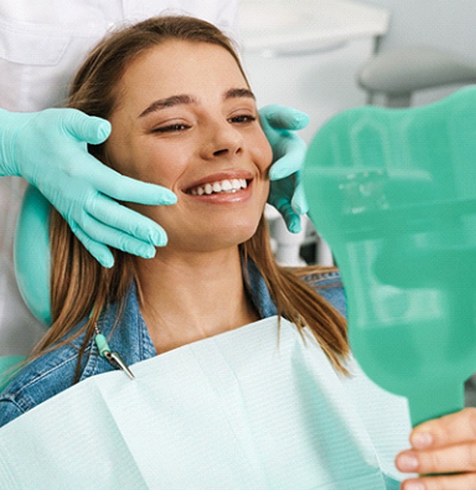 Female patient checking mirror after getting dental implants in Barton City, MI