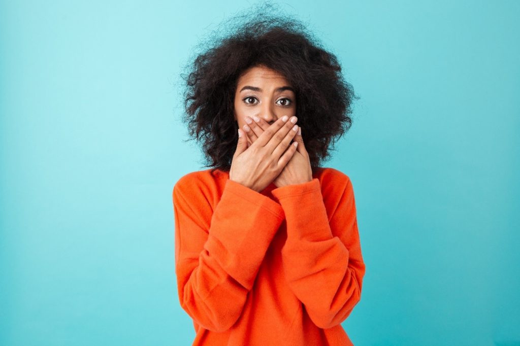 Closeup of woman in orange sweater covering her mouth in shock