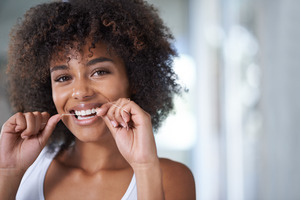 Woman smiling and flossing her teeth while wearing a white shirt